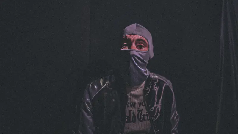 Captain Real Estate, masked and in a leather jacket, staring into the camera out of darkness