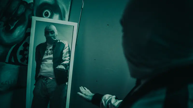 Captain Real Estate reaching toward his own masked reflection in a mirror, in dark teal tones
